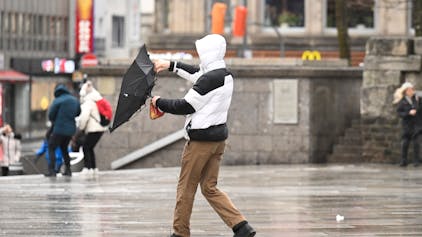 Ein Mann kämpft bei stürmischem Wetter in Köln mit seinem Regenschirm.