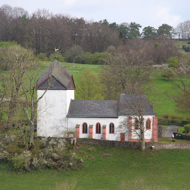 Die Alte Kirche von außen betrachtet: umgeben von Wiesen und einigen Bäumen.