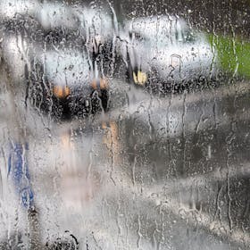 Fahrzeuge sind hinter einer Fensterscheibe zu sehen, auf der sich während eines Unwetters mit Gewitter und Starkregen in Köln-Sülz zahlreiche Regentropfen gesammelt haben. (Symbolbild)