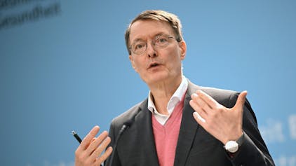Bundesgesundheitsminister Karl Lauterbach (SPD) während einer Pressekonferenz auf einer Bühne. Er trägt ein Sakko und einen lachsfarbenen Pollunder.