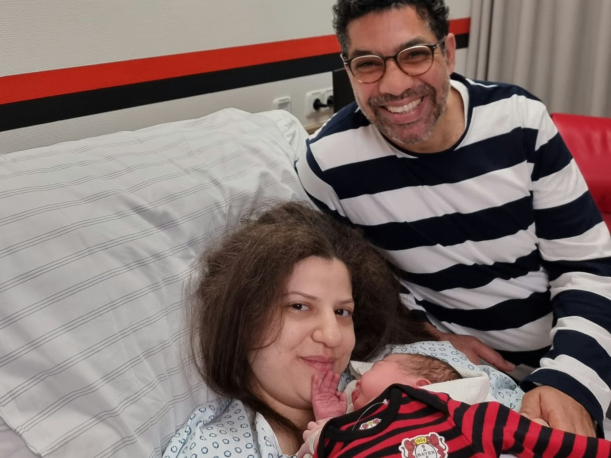 Zwei Eltern auf dem Krankenbett gemeinsam mit ihrem neugeborenen Sohn.
