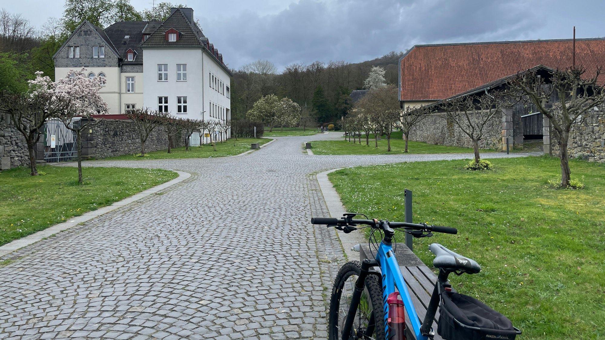 Ein Fahrrad lehnt an einer Bank, im Hintergrund ist das Kloster Heisterbach zu sehen
