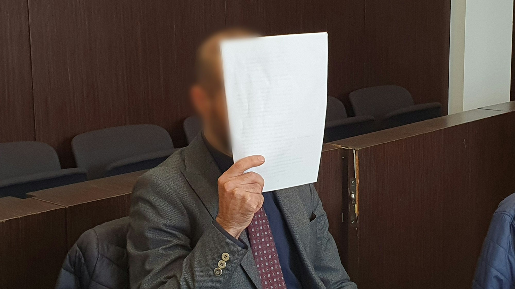 Ein Angeklagter verdeckt sein Gesicht im Gerichtssaal mit einem Blatt Papier.