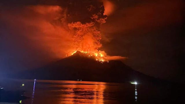 Ein Vulkan stößt bei Dunkelheit dichten Rauch aus, der von austretender Lava auf der Spitze rot erleuchtet wird.