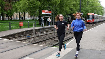 Die Kölnerinnen Katharina Oeltermann und Sophia Staudinger tragen Sportkleidung und laufen an der KVB-Haltestelle Ubierring entlang.
Foto von Martina Goyert




