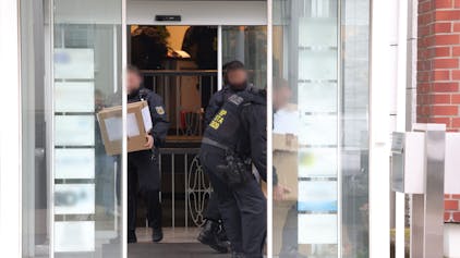 Solingen: Polizeibeamte tragen in Kartons sichergestelltes Material aus einem Gebäude.