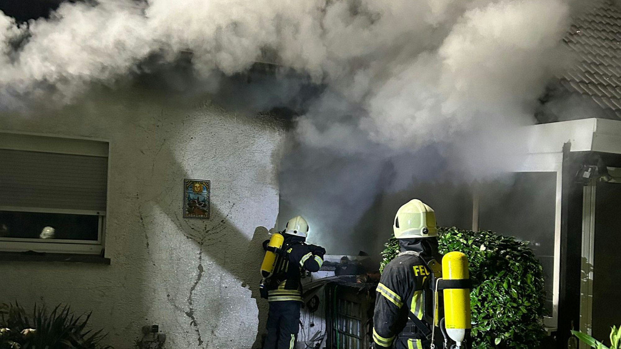 Unter schwerem Atemschutz gehen Feuerwehrleute gegen das Feuer in einem brennenden Haus in Overath-Untereschbach vor.