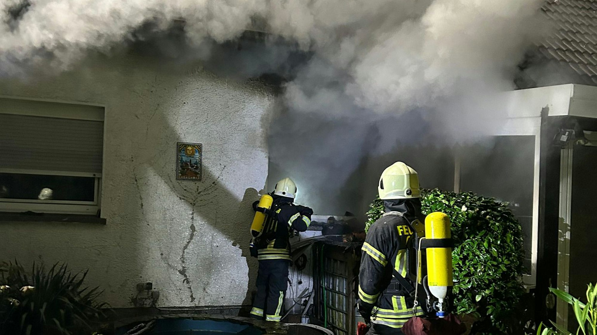 Feuerwehrleute löschen ein Haus, aus dem dunkler Rauch quillt.