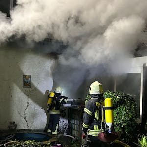 Unter schwerem Atemschutz gehen Feuerwehrleute gegen das Feuer in einem brennenden Haus in Overath-Untereschbach vor.