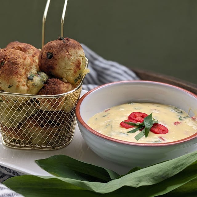 Kartoffel-Bärlauch-Bällchen stehen in einem Körbchen neben einer Schüssel mit Sauce Hollandaise-Dip.