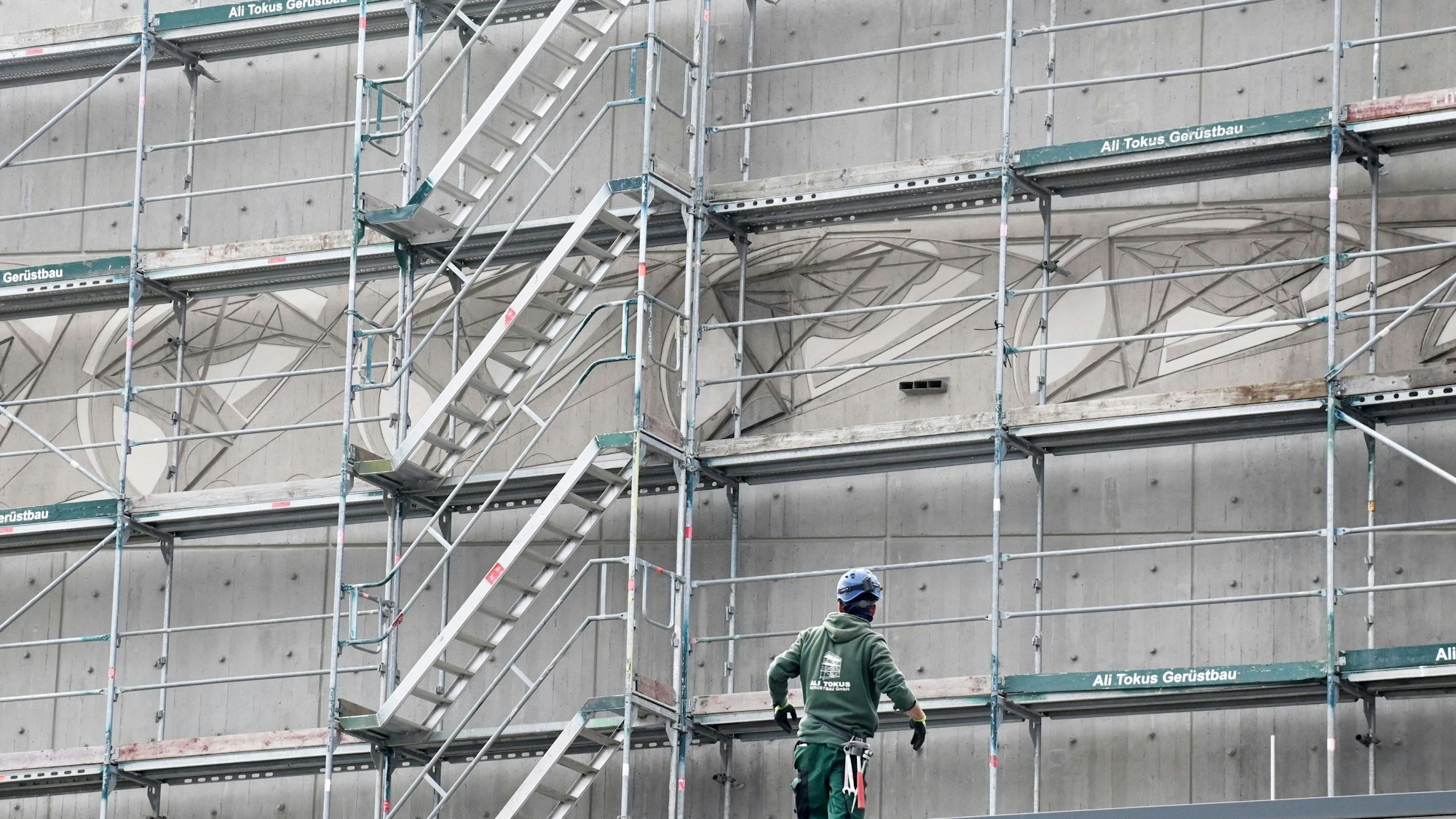 Ein Bauarbeiter ist vor einem Baugerüst zu sehen. Dahinter zeichnet sich das kunstvolle Relief auf der Fassade ab.