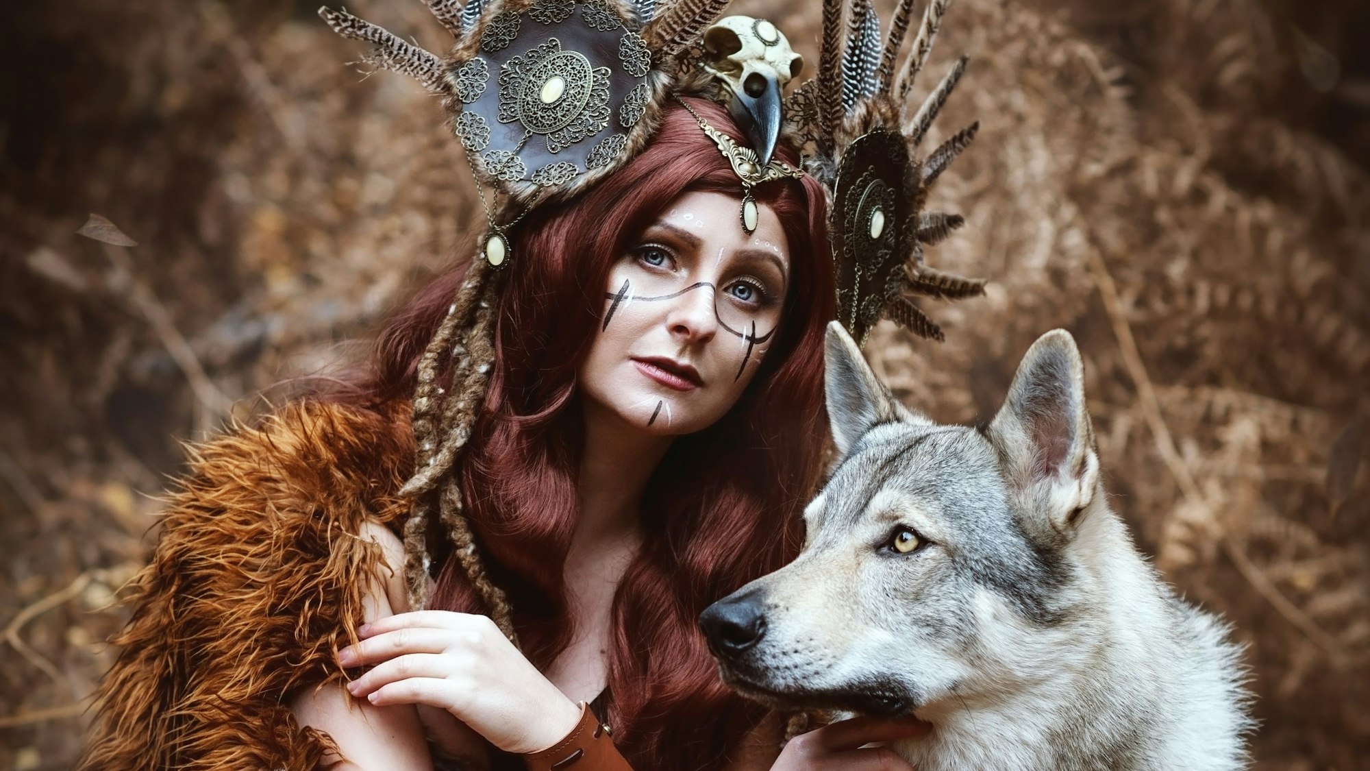 Eine junge Frau trägt schamanisch anmutenden Kopfschmuck und posiert mit einem Wolf.