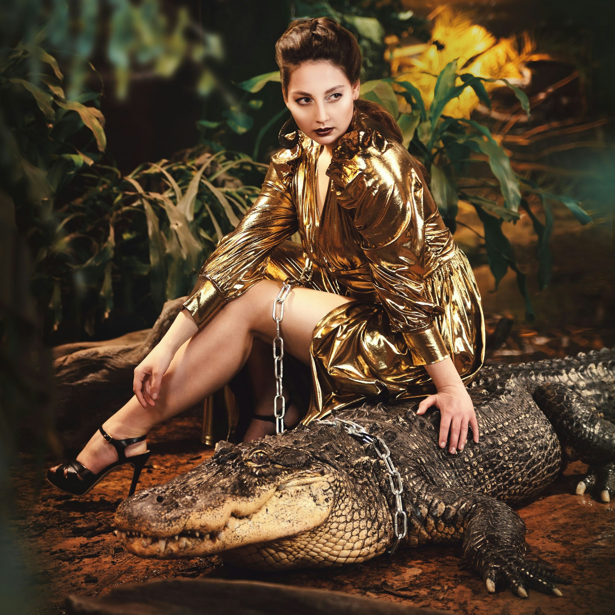 Julia Katharina Stark trägt ein goldenes Kleid und posiert mit einem Krokodil, um das eine Kette wie eine Leine gelegt ist.