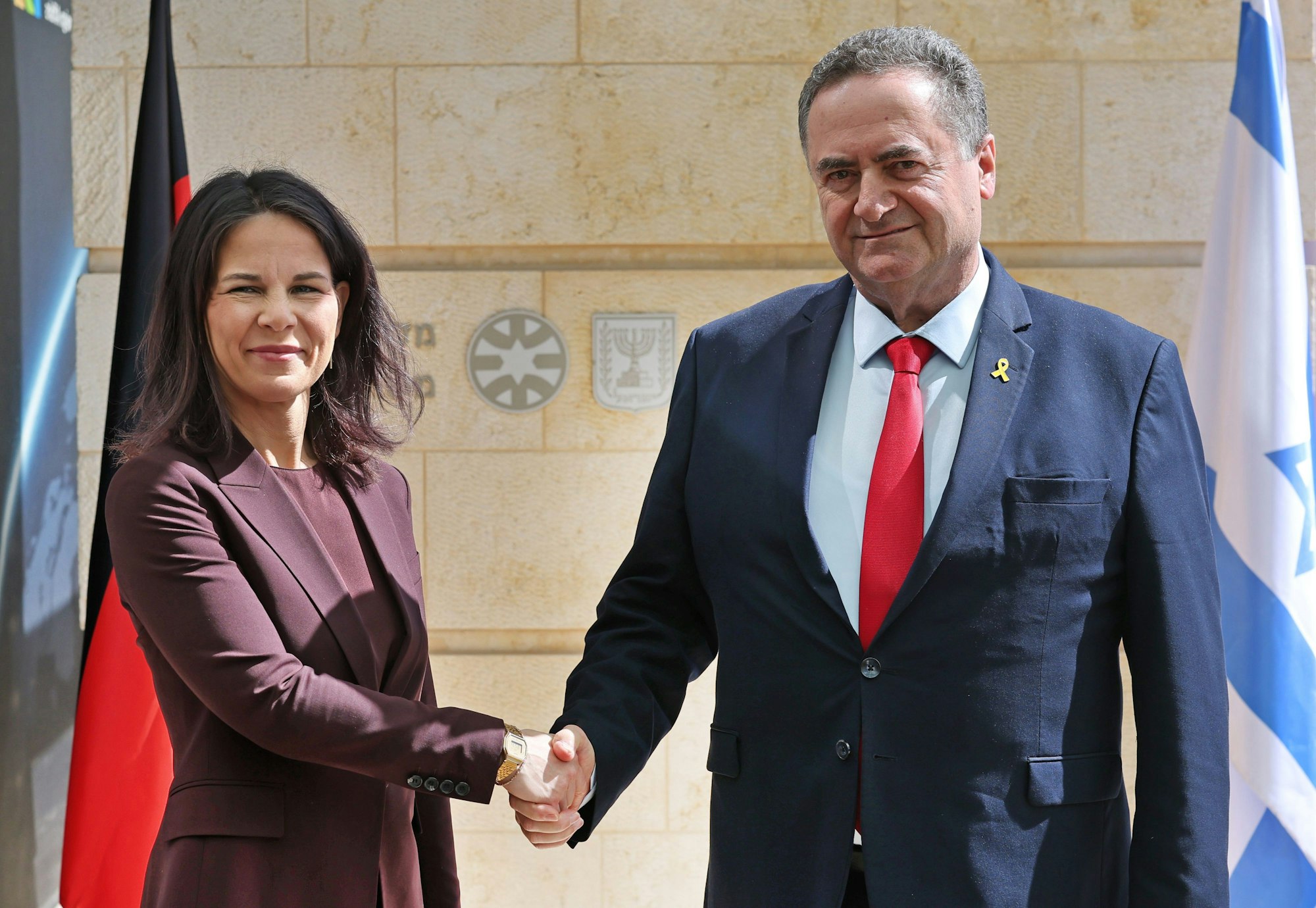 Der israelische Außenminister Israel Katz (r) schüttelt der deutschen Außenministerin Annalena Baerbock (l, Bündnis90/Grüne) vor den jeweiligen Landesflaggen die Hand.
