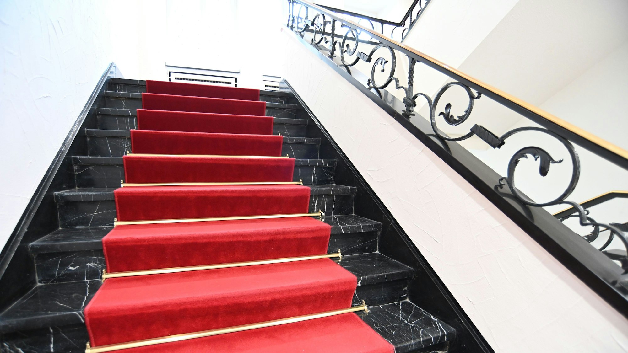 Ein roter Teppich läuft über eine schwarze Marmortreppe ins Obergeschoss.
