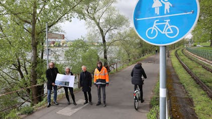 Eine vierköpfige Gruppe steht auf einem Radweg, am Rand weisen rot-weiße Schilder nach Bonn und Königswinter..
