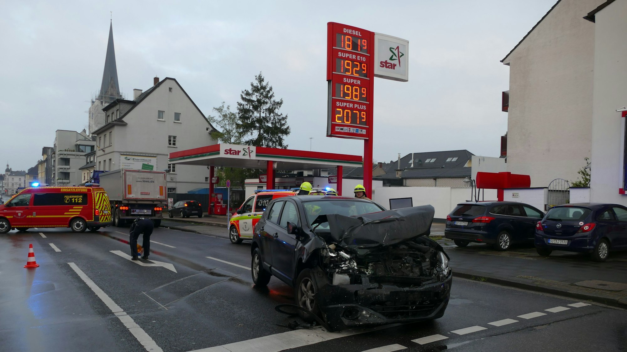 Ein kaputtes Auto steht auf einer Straße vor einer Tankstelle.