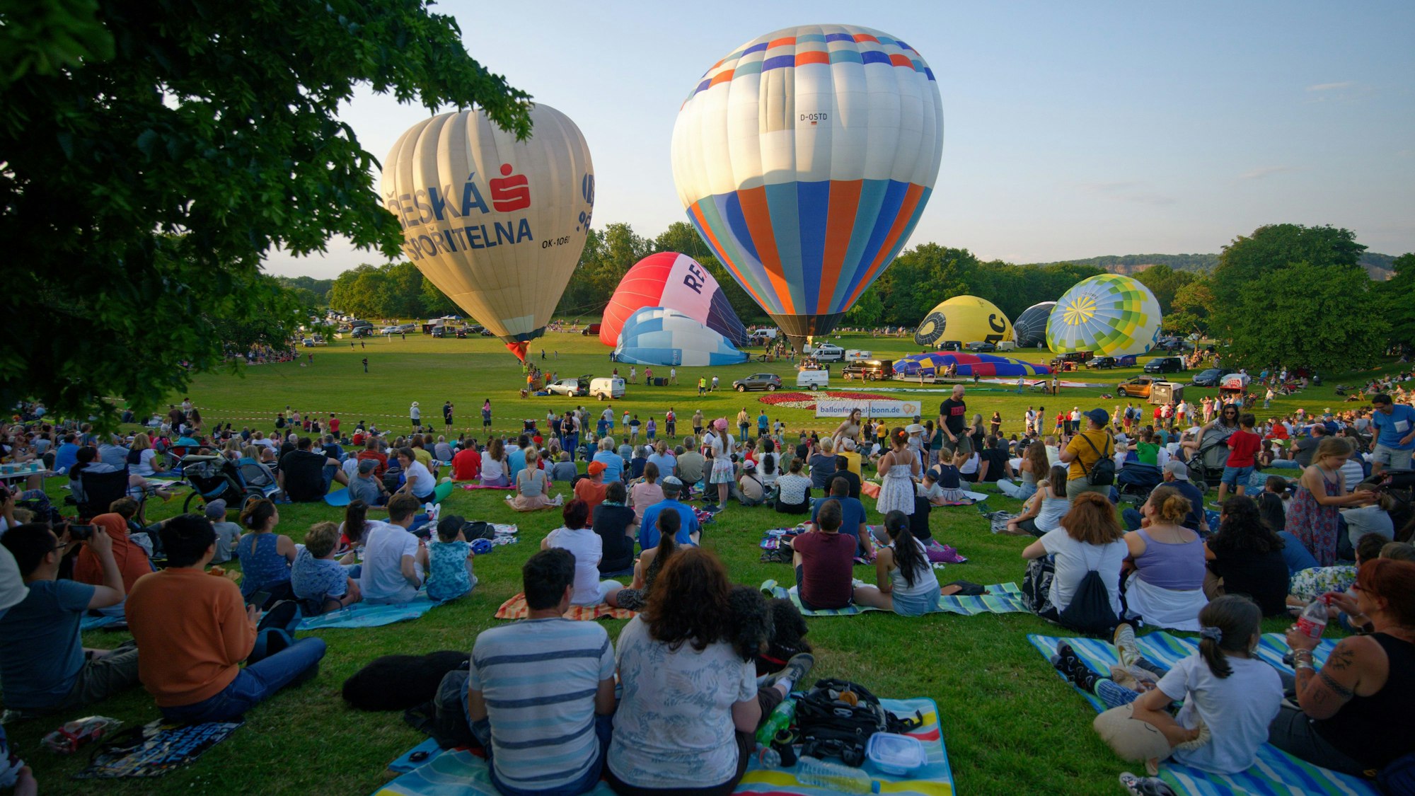 Zuschauer verfolgen den Start von etlichen Heißluftballons.