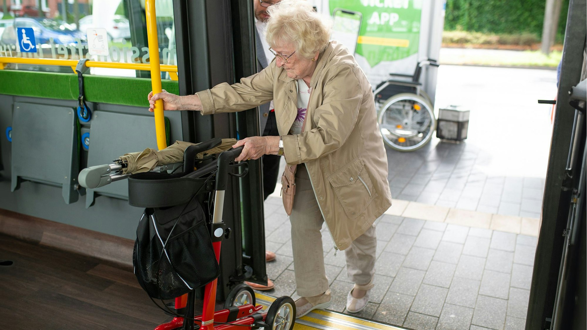 Eine Frau mit Rollator steigt an einer barrierefreien Bushaltestelle in den Bus ein.