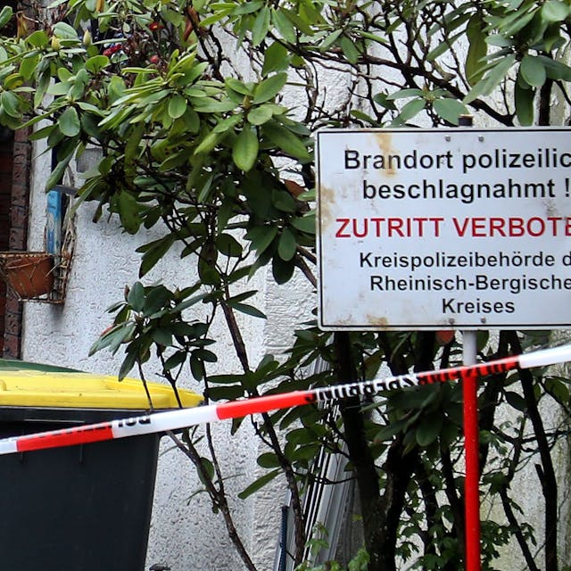 Vor einem Haus steht ein Schild mit der Aufschrift „Brandort polizeilich beschlagnahmt! Zutritt verboten“. Davor ist Polizei-Absperrband zu sehen.