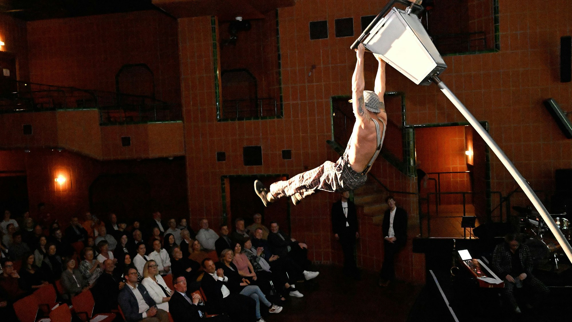 Ein Mann hängt an einer Laterne über dem Publikum im großen Saal des Bergischen Löwen.