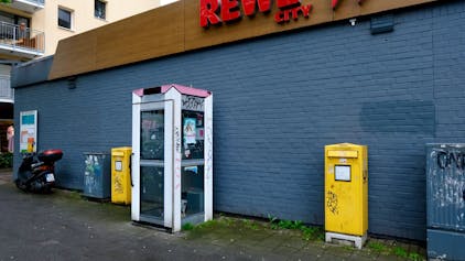 Das Bild zeigt eine verwahrloste und nicht mehr funktionstüchtige Telefonzelle vor dem Rewe-Markt an der Dürener Straße. Foto von Susanne Esch