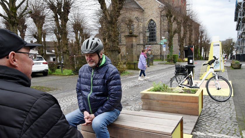 Zwei Männer sitzen auf neuen Bänken an einer Straße in Lindlar.