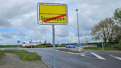 Ein Schild zeigt das Ende eines Gewerbeparks an, dahinter fahren Autos und ein Lastwagen durch einen Verkehrskreisel.