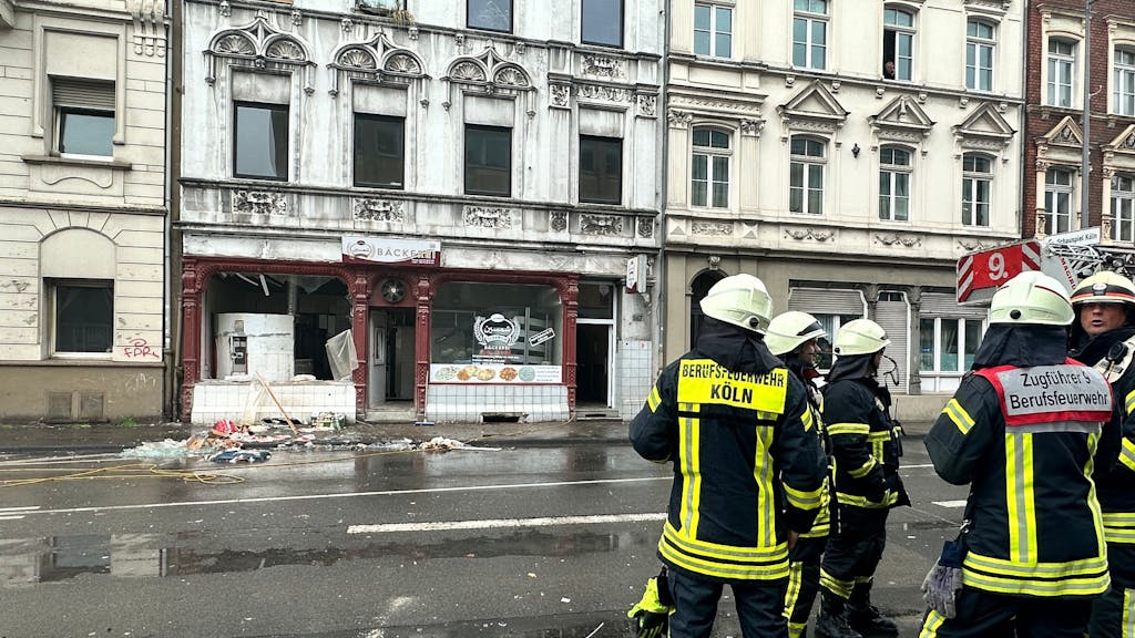 Einsatzkräfte der Feuerwehr Köln stehen vor einer Bäckerei, deren Schaufenster zerborsten sind.&nbsp;