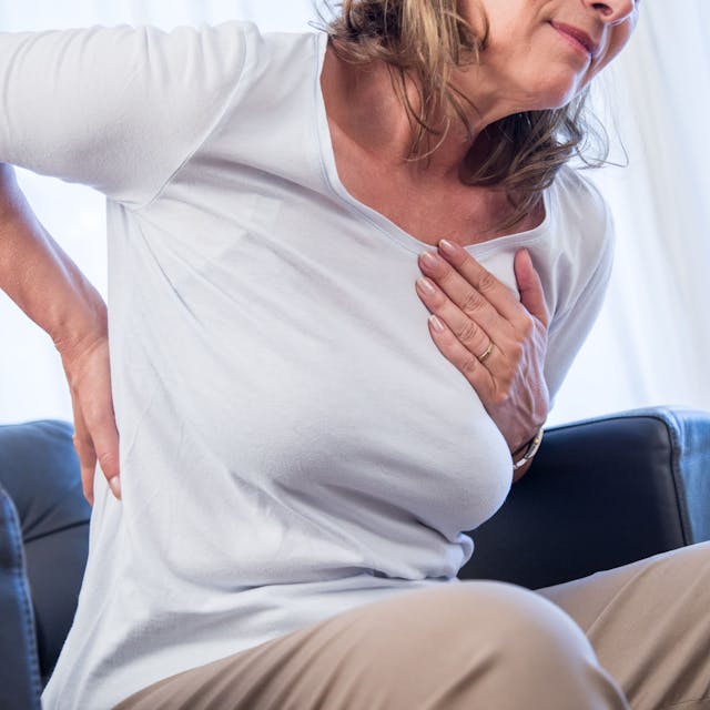 Eine Frau hält sich die Hände an Brustkorb und Rücken, als hätte sie Schmerzen