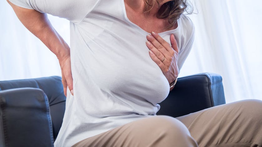 Eine Frau hält sich die Hände an Brustkorb und Rücken, als hätte sie Schmerzen