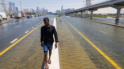 Ein Mann läuft über eine Mauer zwischen zwei überfluteten Straßen in Dubai. Experten halten Cloud Seeding nicht für den Grund für die heftigen Regenfälle in den Vereinigten Arabischen Emiraten.