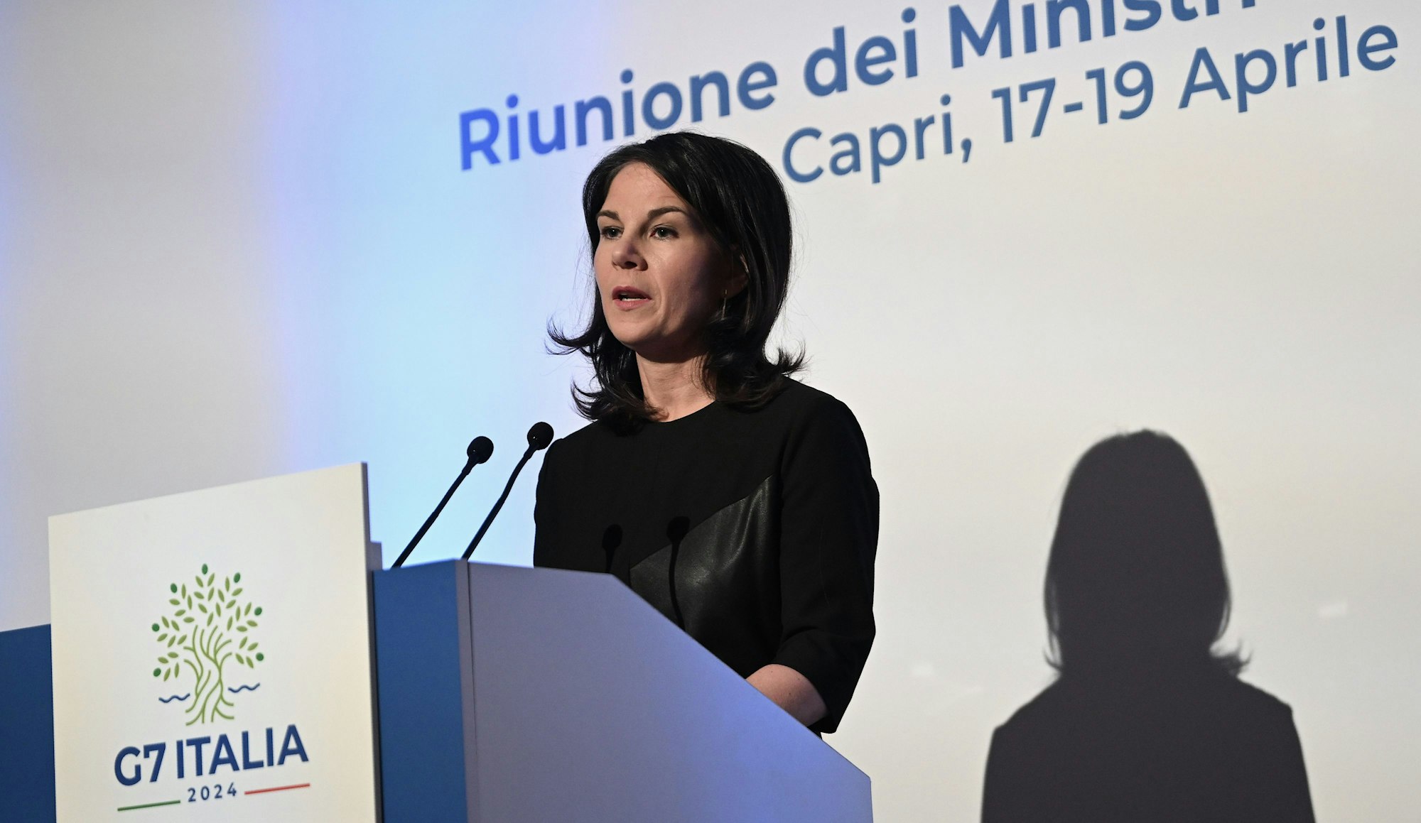 Capri: Annalena Baerbock (Bündnis 90/Die Grünen), Bundesministerin des Auswärtigen, spricht in zwei Mikrofone. Sie wird angeleuchtet und wirft einen Schatten auf einen weißen Hintergrund.