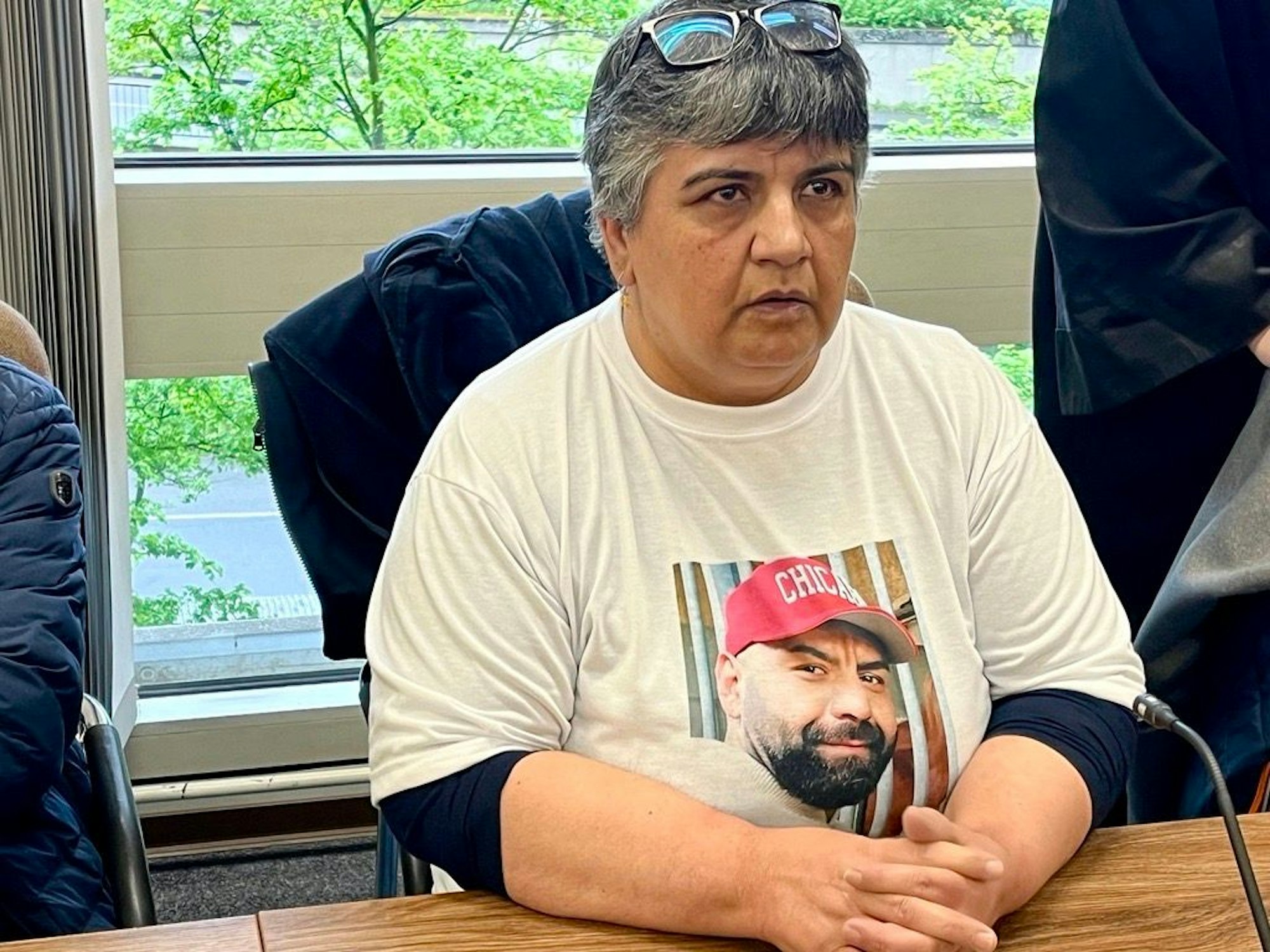 Eine Frau sitzt in einem Gerichtssaal und trägt ein T-Shirt mit dem Foto eines jungen Mannes.