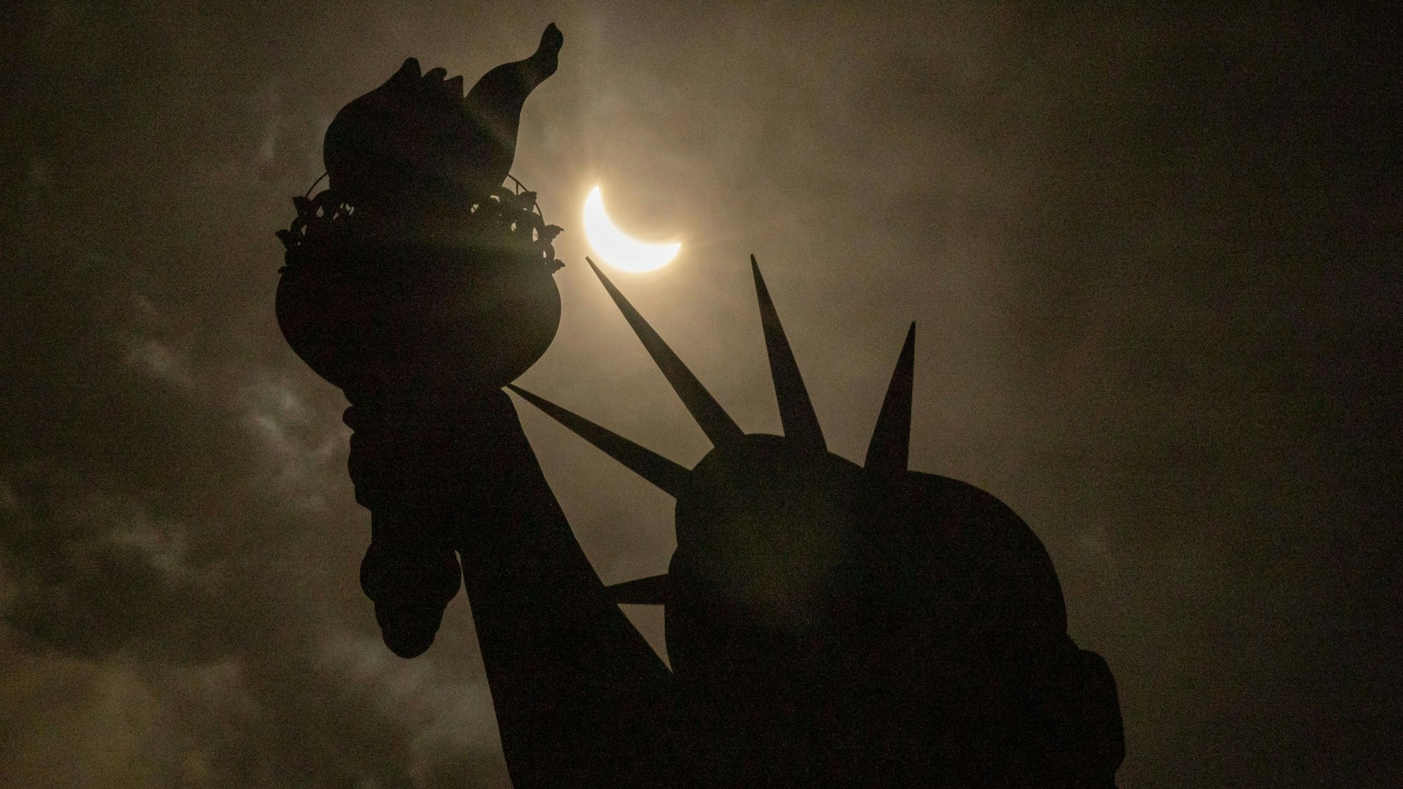 8, April 2024, USA, New York: Der Mond verdeckt teilweise die Sonne hinter der Freiheitsstatue während der totalen Sonnenfinsternis auf Liberty Island.