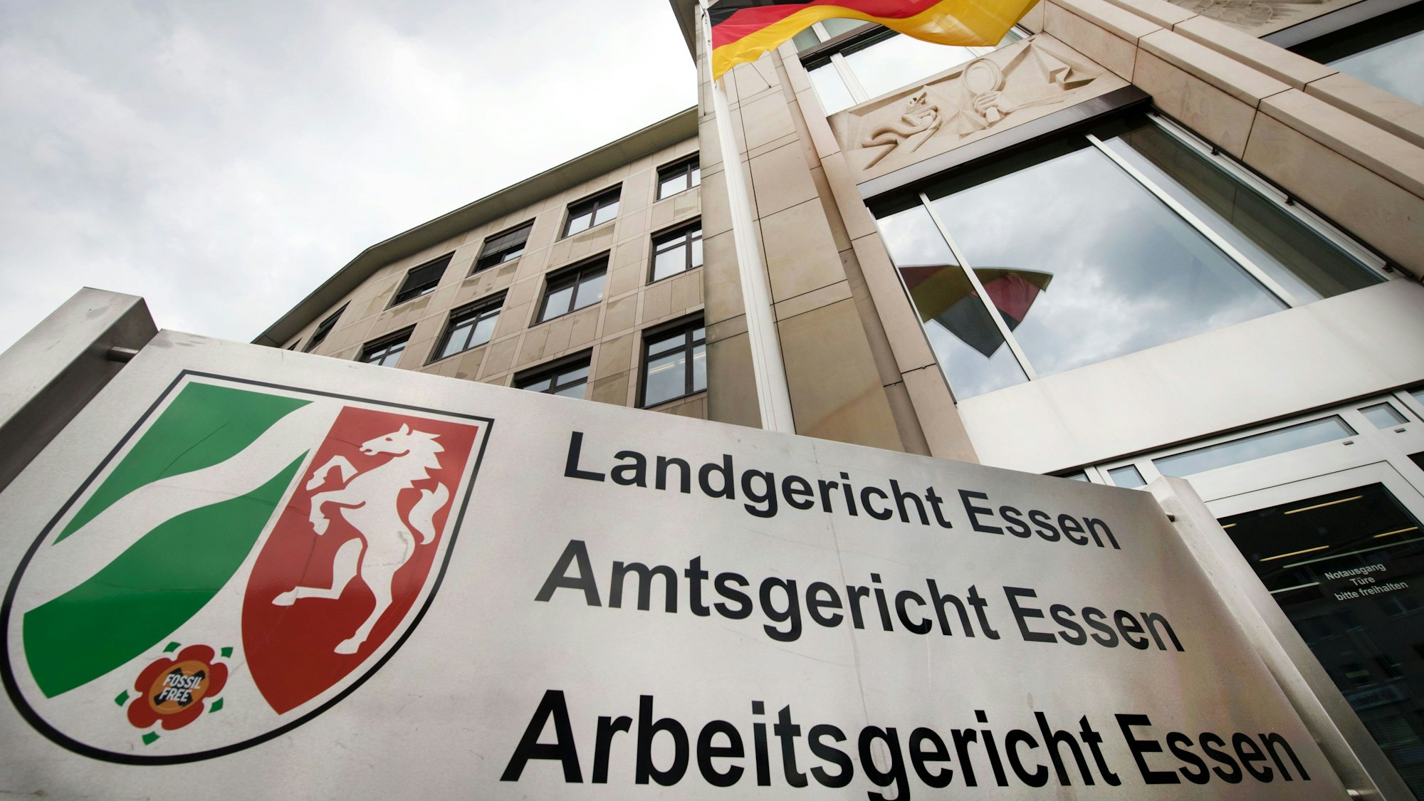 Aufnahme des Landgericht Essen aus der Froschperspektive - im Hintergrund weht eine Deutschlandfahne unter einem bewölkten Himmel.