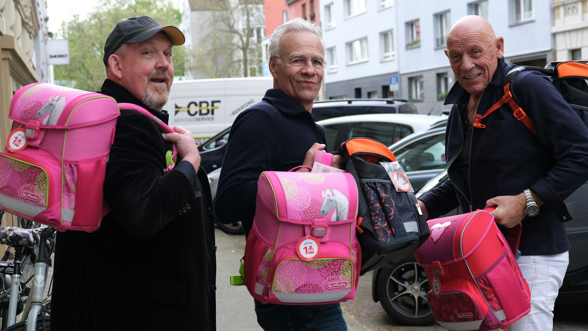Die Schauspieler Dietmar Bär, Klaus J. Behrendt und Joe Bausch halten vier von insgesamt 774 hochwertigen Schulranzen, die der Kölner „Tatort-Verein“ an arme Kinder spendet, in der Hand.