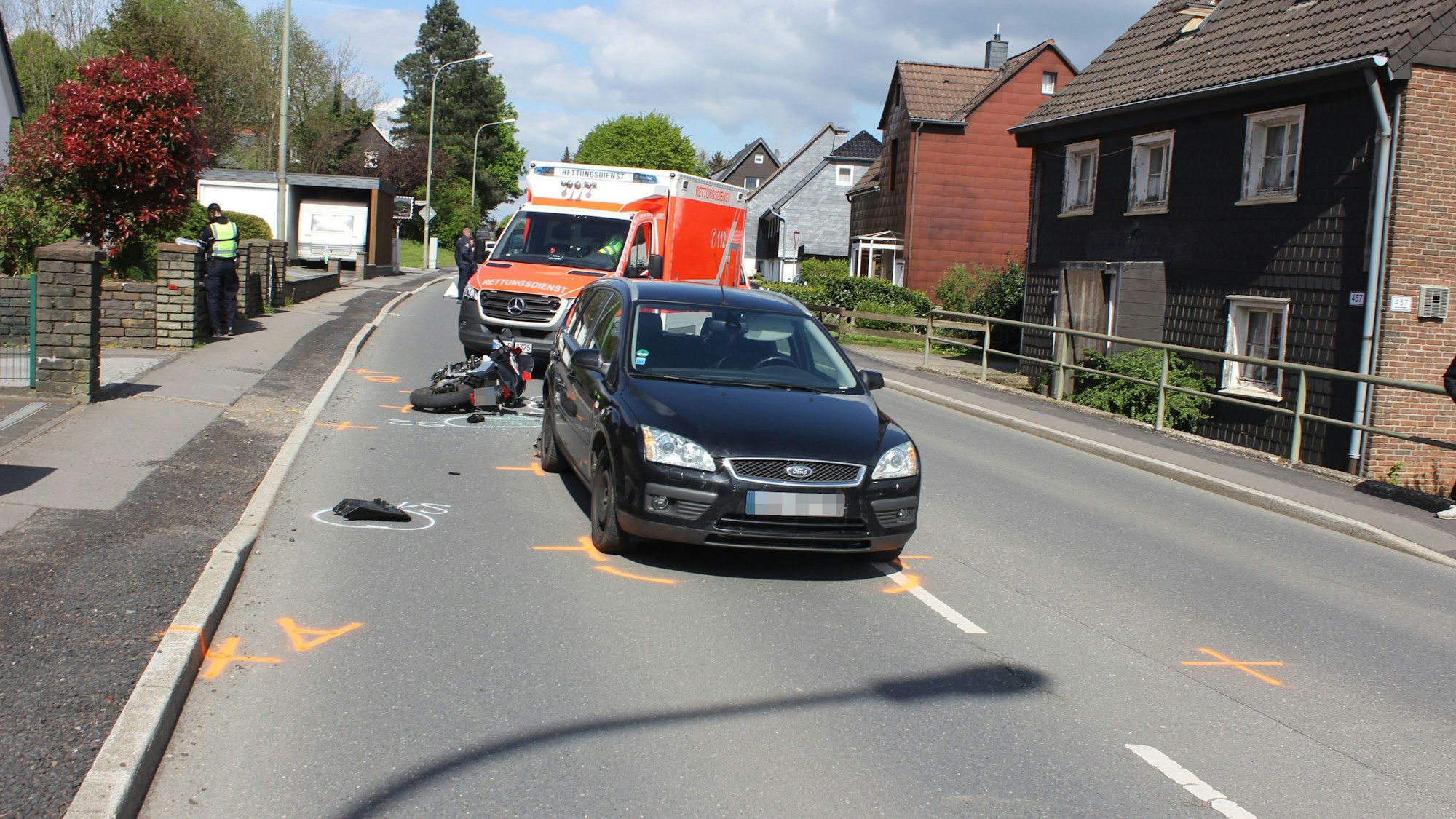 EIn Auto steht auf der Straße. Dahinter liegt ein beschädigter Motorroller vor einem Krankenwagen.