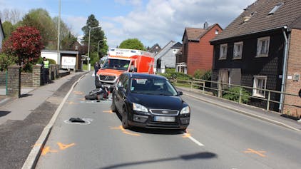 EIn Auto steht auf der Straße. Dahinter liegt ein beschädigter Motorroller vor einem Krankenwagen.