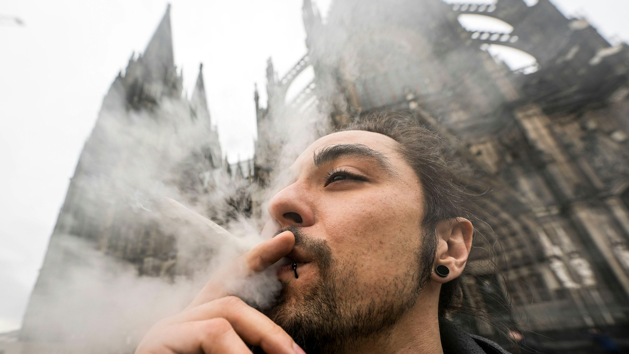 Ein Mann raucht vor dem Kölner Dom einen Joint.