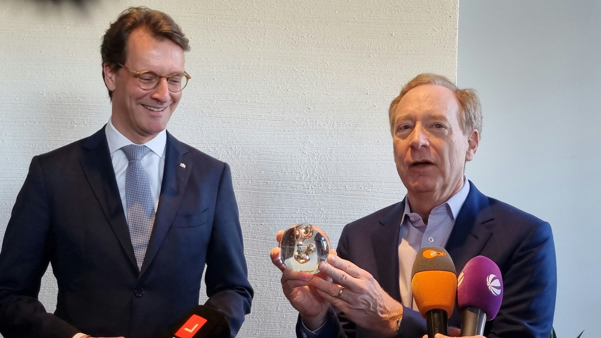 NRW-Ministerpräsident Hendrik Wüst (links) hat Microsoft-Vize Brad Smith flüssige, in Glas eingefasste Kohle als Geschenk mitgebracht.