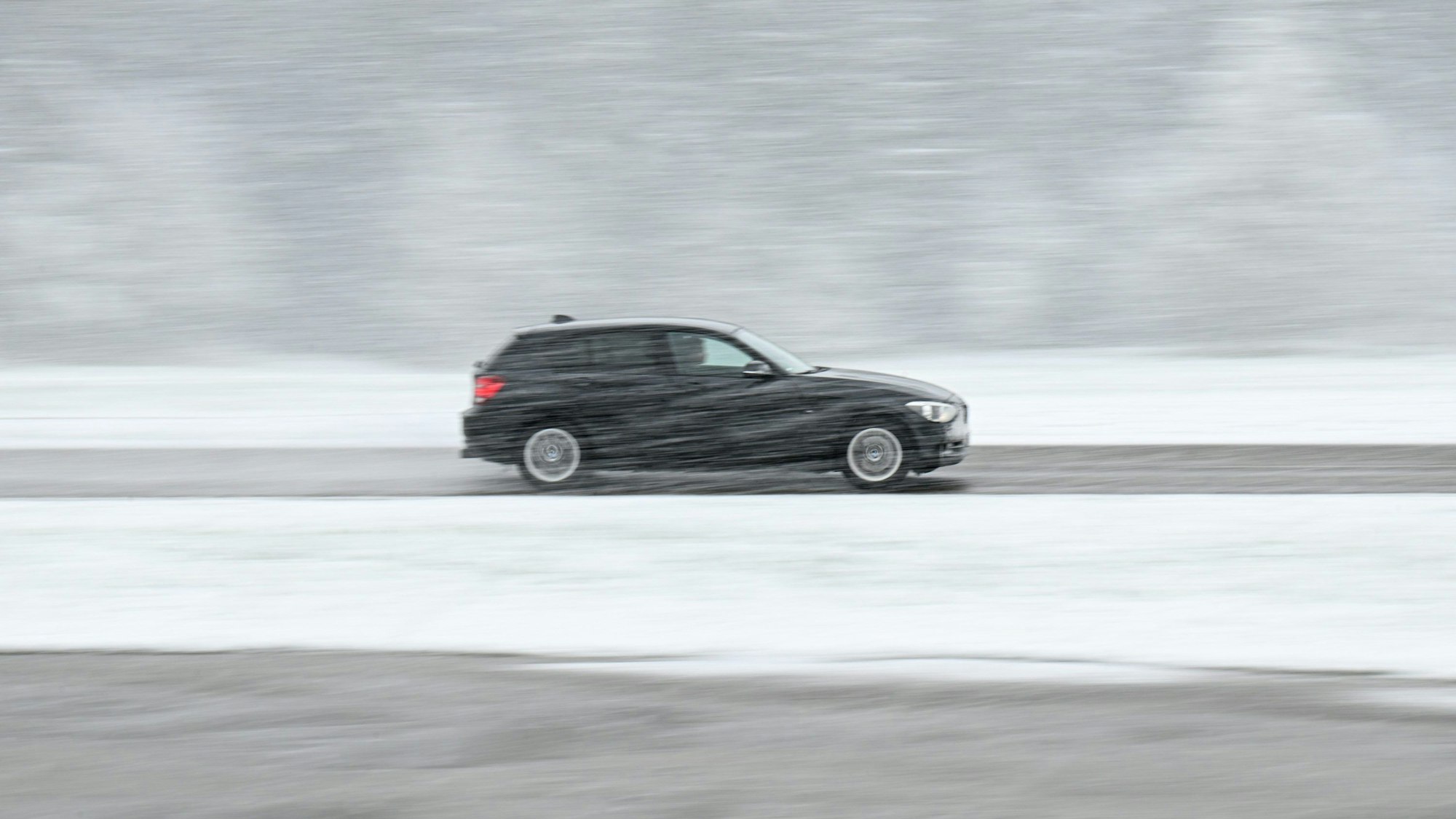 Ein schwarzer Wagen fährt über eine teils schneebedeckte Landesstraße bei Böhmenkirch.