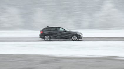 Ein schwarzer Wagen fährt über eine teils schneebedeckte Landesstraße bei Böhmenkirch.&nbsp;
