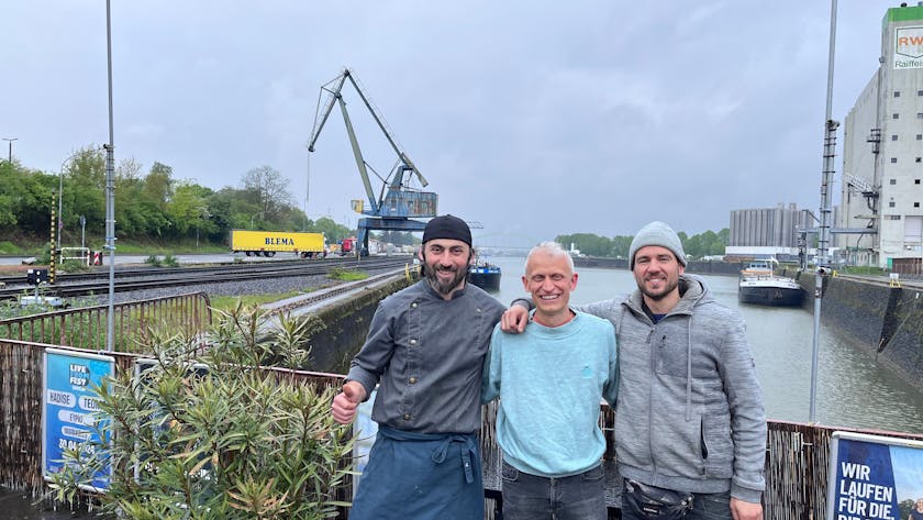 Erkan Karakas, Inhaber der Erkantine, Philip Minettos vom Verein Rosarot und Unterstützer Mario Sroka freuen sich auf das „Vrühlingsfest“ am Niehler Hafen.