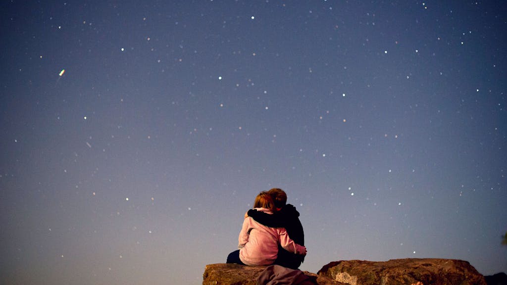Ein Paar sitzt auf einem Felsen und schaut in den Nachthimmel.