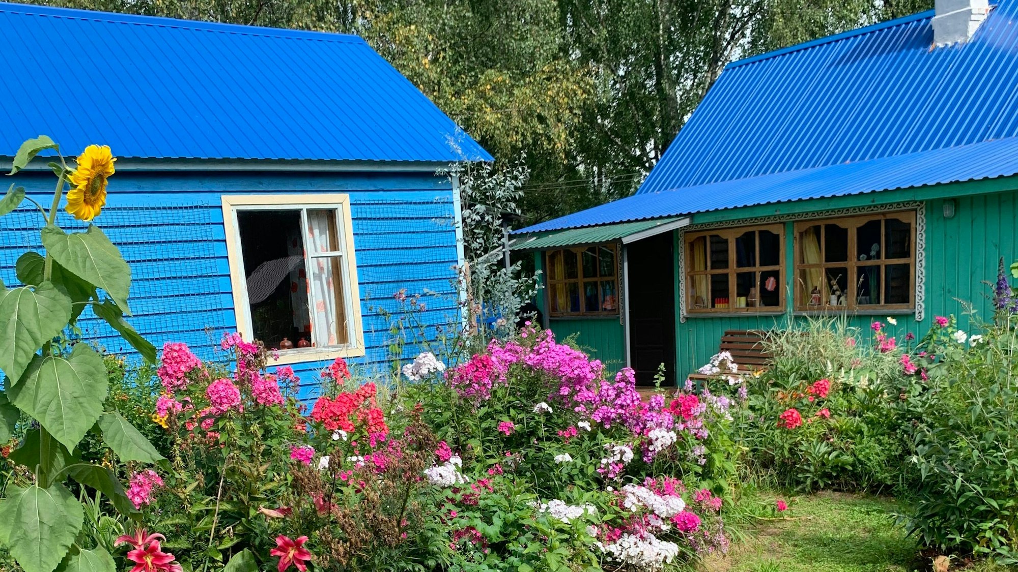 Zwei kleine blau/türkise Holzhütten in einem Blumengarten.