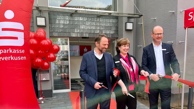 OB Uwe Richrath, Filialleiterin Heike Schulz und Sparkassenvorstand Markus Grawe schneiden vor der umgebauten Filiale in Lützenkirchen ein rotes Band durch.