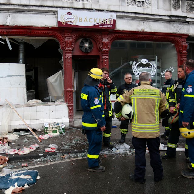 Brandermittler und Feuerwehleute stehen vor einer Bäckerei, die durch die Verpuffung zerstört wurde.