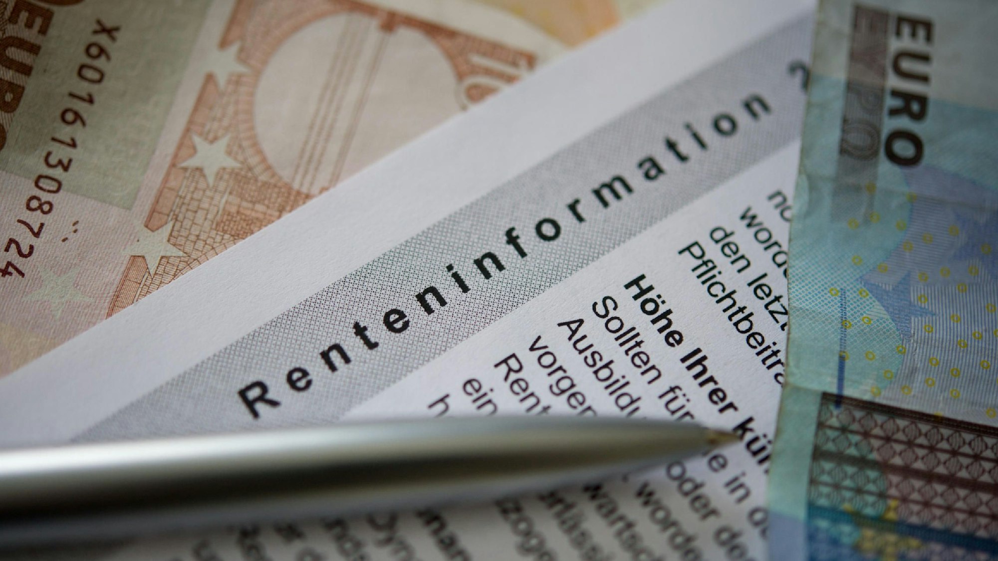 Ein Kugelschreiber und ein Geldschein liegen auf einer Renteninformation, dem jährlichen Schreiben der Deutschen Rentenversicherung an alle Versicherten zu ihrer gesetzlichen Rente.