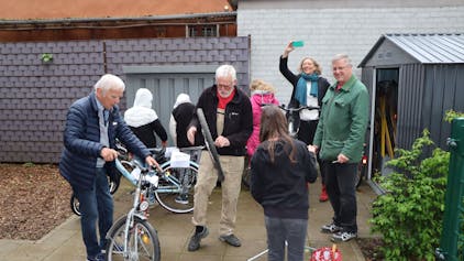 Ehrenamtler vom Repair-Café reparieren zwei Fahrräder. Schülerinnen und Schüler helfen dabei mit.